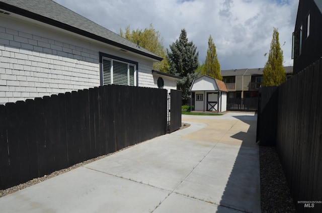 view of property exterior with roof with shingles, a storage shed, an outdoor structure, a fenced backyard, and a patio