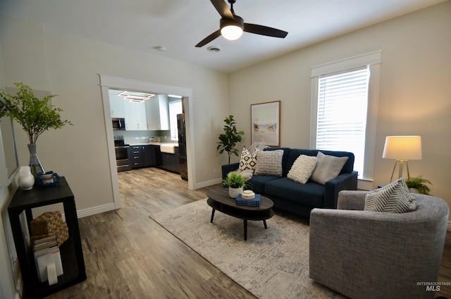 living room featuring baseboards, a ceiling fan, light wood finished floors, and visible vents