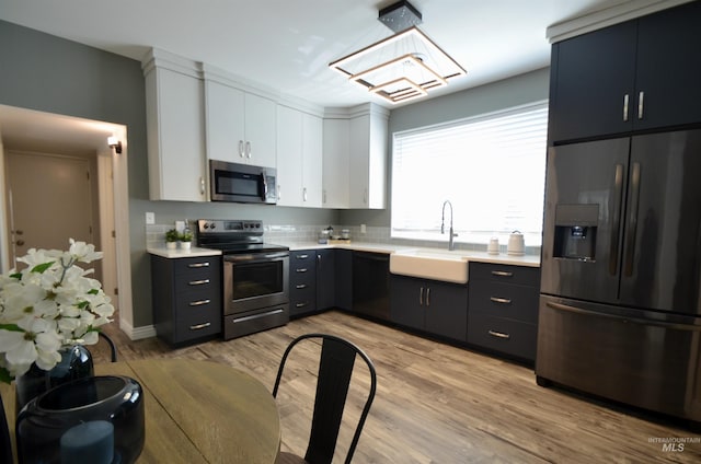 kitchen with light countertops, white cabinetry, a sink, light wood finished floors, and stainless steel appliances