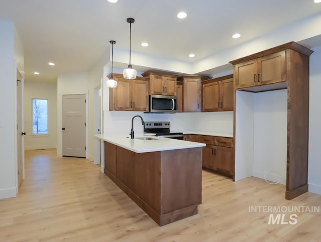 kitchen featuring brown cabinets, light countertops, hanging light fixtures, appliances with stainless steel finishes, and light wood-type flooring