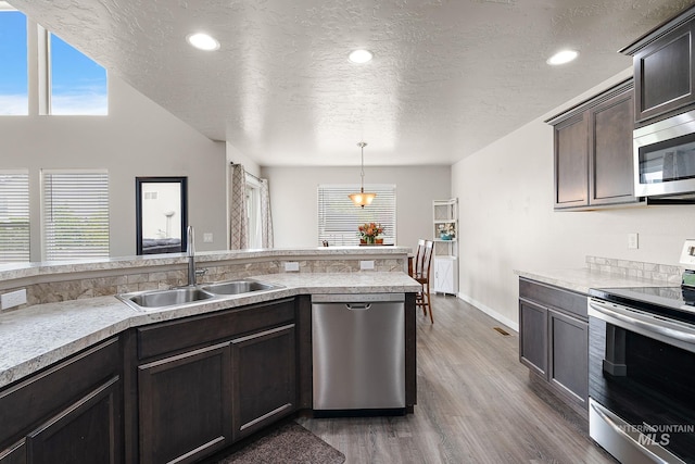 kitchen featuring wood finished floors, light countertops, a textured ceiling, a sink, and appliances with stainless steel finishes