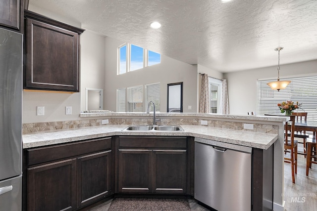 kitchen featuring dark brown cabinets, appliances with stainless steel finishes, a sink, a textured ceiling, and a peninsula