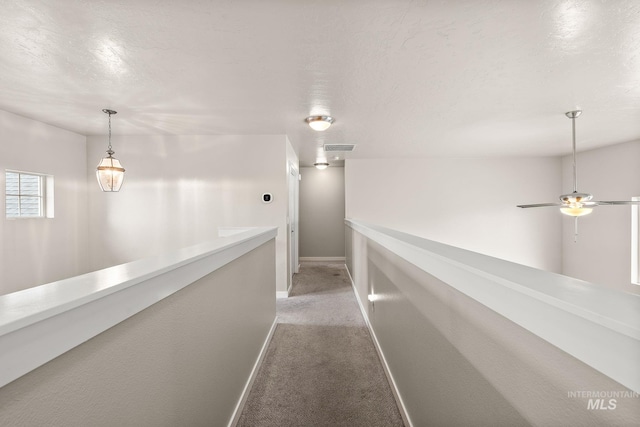 hallway with visible vents, light carpet, baseboards, a textured ceiling, and an upstairs landing
