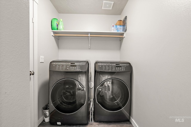 laundry area with laundry area, visible vents, wood finished floors, baseboards, and washing machine and clothes dryer