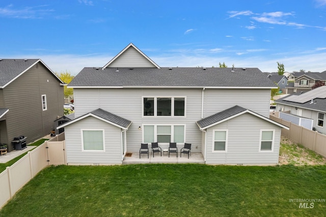 rear view of house featuring a fenced backyard, a shingled roof, a lawn, and a patio area