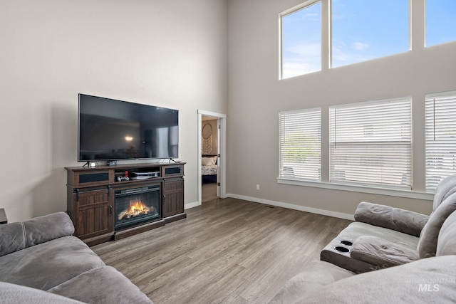 living area with baseboards, a high ceiling, a glass covered fireplace, and wood finished floors