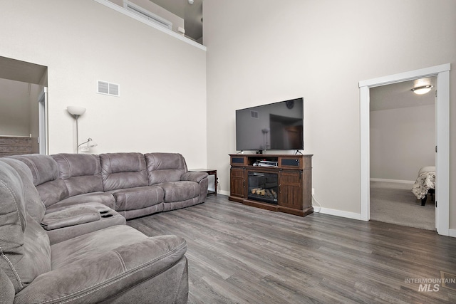 living area featuring baseboards, visible vents, wood finished floors, and a towering ceiling