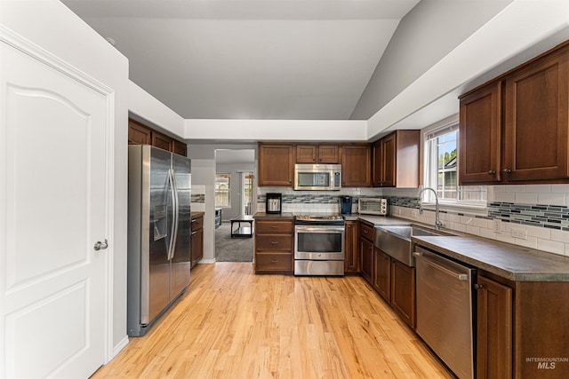 kitchen with decorative backsplash, dark countertops, light wood-style floors, a sink, and appliances with stainless steel finishes