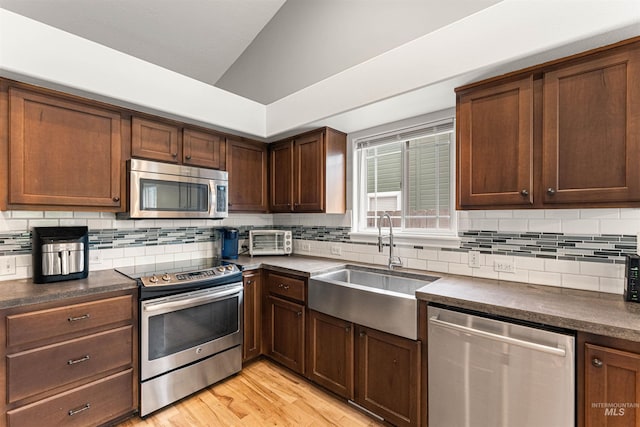 kitchen featuring dark countertops, a sink, stainless steel appliances, backsplash, and vaulted ceiling