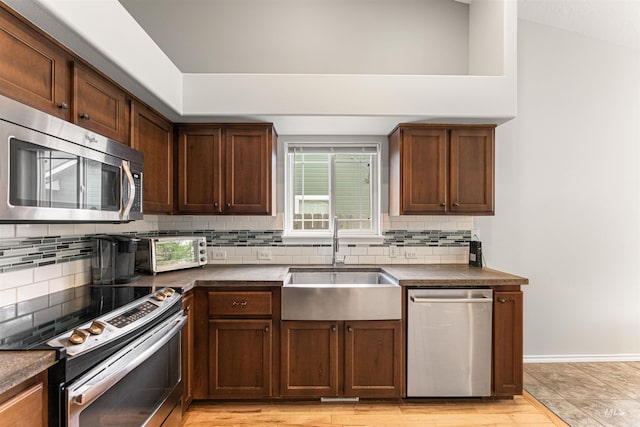 kitchen with decorative backsplash, appliances with stainless steel finishes, dark countertops, a sink, and a toaster