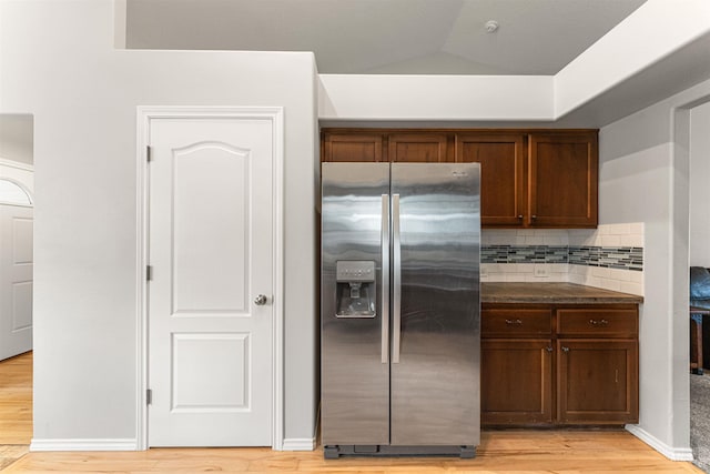 kitchen with stainless steel refrigerator with ice dispenser, vaulted ceiling, decorative backsplash, and light wood-type flooring
