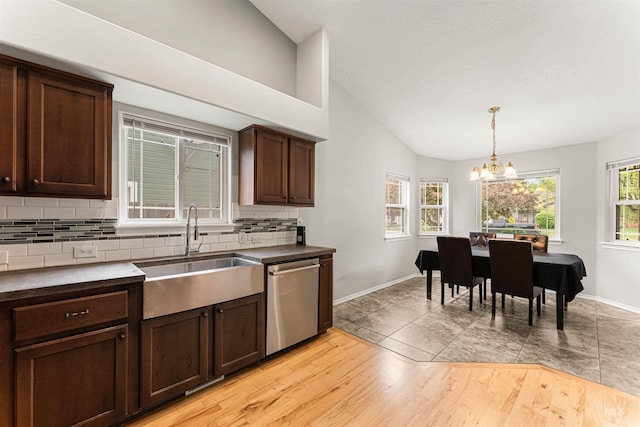 kitchen featuring stainless steel dishwasher, dark countertops, tasteful backsplash, a sink, and vaulted ceiling