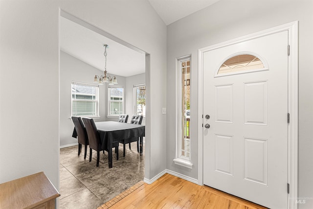 foyer with baseboards, a notable chandelier, light wood finished floors, and lofted ceiling