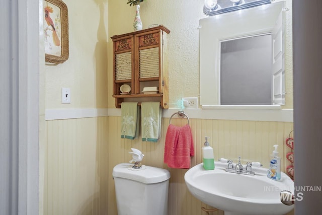 half bath featuring wainscoting, a sink, and toilet