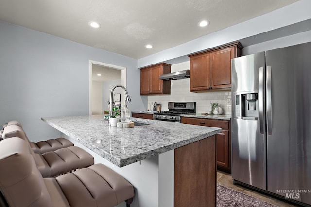 3209 W Plant Dr, Boise, ID 83703 - kitchen featuring stainless steel appliances, exhaust hood, a breakfast bar area, a sink, and decorative backsplash