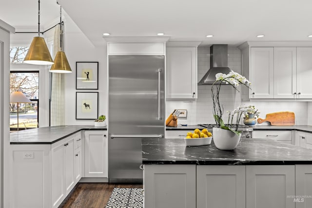 kitchen with dark wood finished floors, white cabinetry, stainless steel appliances, and wall chimney range hood