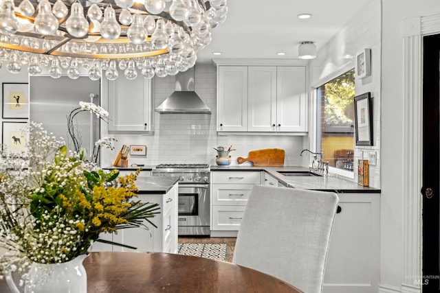 kitchen featuring high end stainless steel range, a sink, dark countertops, wall chimney range hood, and decorative backsplash