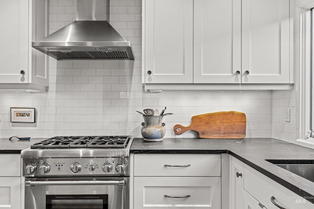 kitchen featuring white cabinetry, backsplash, stainless steel stove, and wall chimney range hood