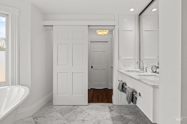 bathroom with baseboards, double vanity, a soaking tub, marble finish floor, and a sink