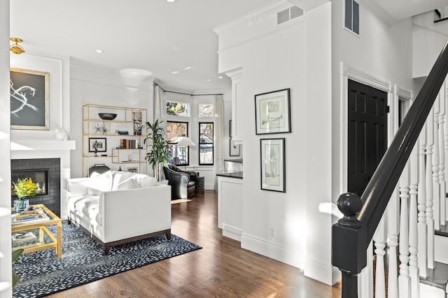 living room with visible vents, ornamental molding, a glass covered fireplace, dark wood-style floors, and stairs