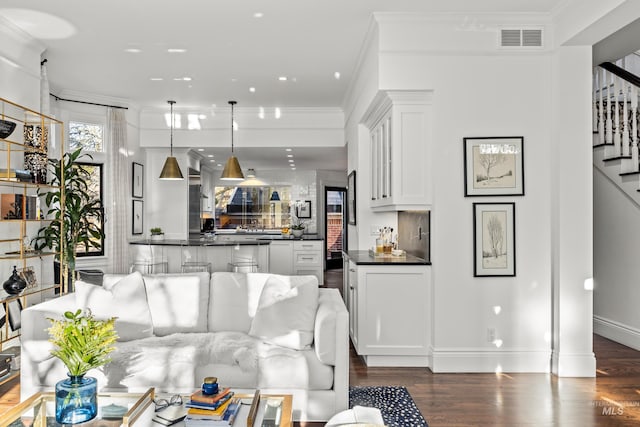 living room with stairs, visible vents, dark wood-type flooring, and crown molding