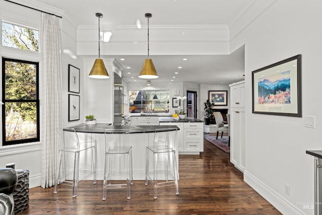 kitchen featuring dark countertops, a peninsula, dark wood-type flooring, white cabinetry, and crown molding