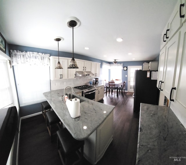 kitchen featuring a breakfast bar area, decorative light fixtures, black refrigerator, stainless steel range with gas cooktop, and light stone countertops