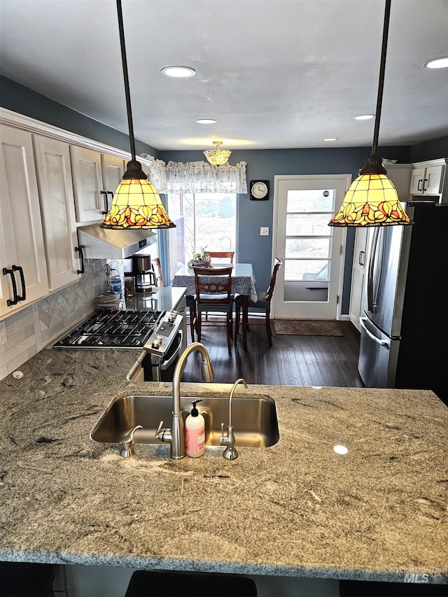 kitchen featuring sink, backsplash, stainless steel appliances, light stone countertops, and decorative light fixtures