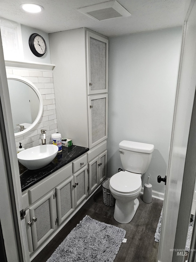 bathroom featuring wood-type flooring, backsplash, vanity, toilet, and a textured ceiling