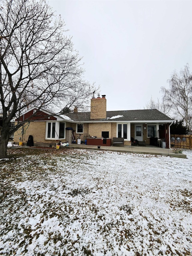 snow covered back of property with a jacuzzi and a patio area