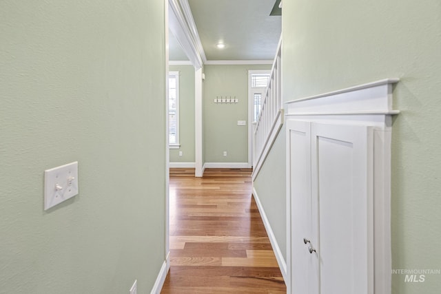 corridor with ornamental molding, stairs, baseboards, and wood finished floors