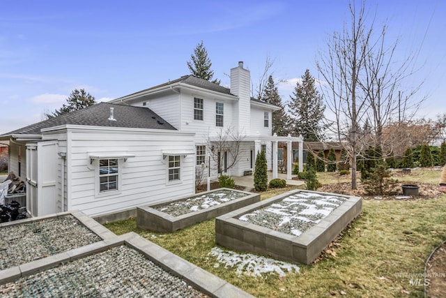 back of property featuring a chimney, a vegetable garden, and roof with shingles