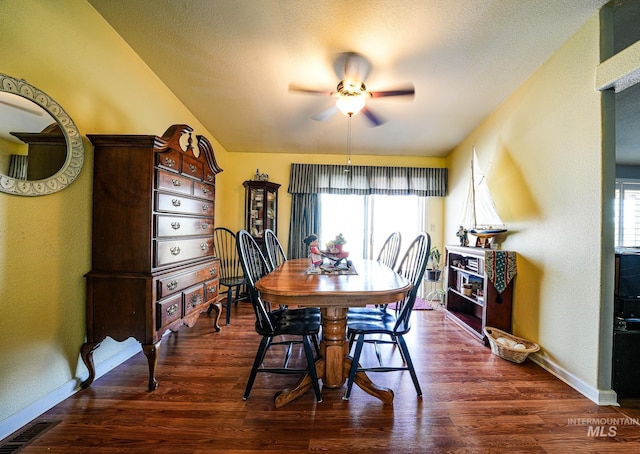 dining space featuring a textured wall, dark wood-type flooring, a ceiling fan, a textured ceiling, and baseboards