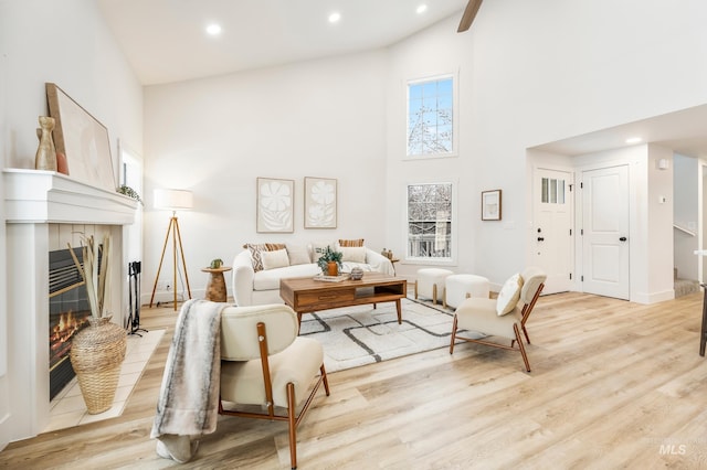 living room with a high ceiling, a tile fireplace, and light hardwood / wood-style floors