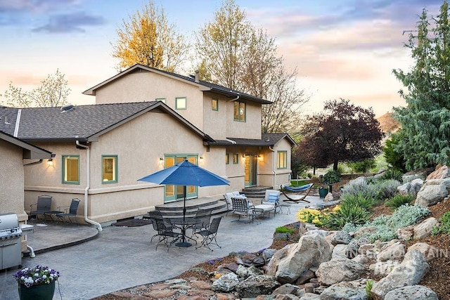 back of house at dusk featuring stucco siding and a patio area
