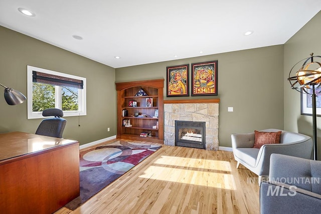 office area with baseboards, recessed lighting, wood finished floors, and a stone fireplace