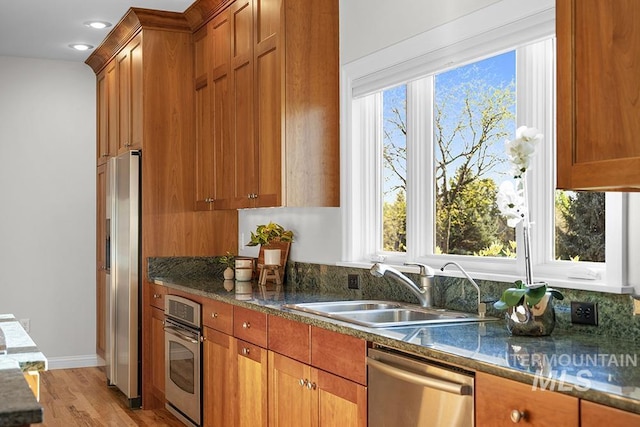 kitchen featuring light wood-type flooring, brown cabinets, a sink, dark stone countertops, and stainless steel appliances