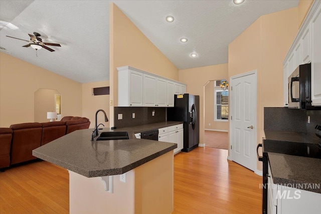 kitchen with dark countertops, open floor plan, a peninsula, black appliances, and a sink