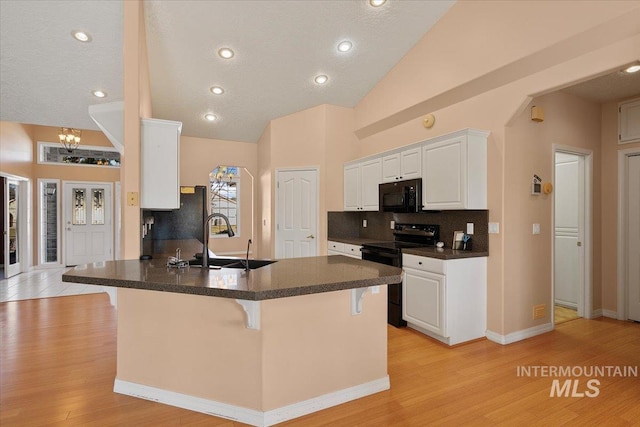 kitchen with a breakfast bar area, a sink, light wood-type flooring, black appliances, and dark countertops