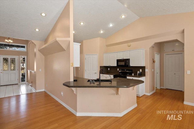 kitchen with arched walkways, a kitchen breakfast bar, a peninsula, black appliances, and a sink