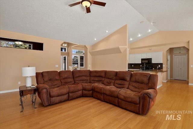 living room with lofted ceiling, light wood finished floors, a ceiling fan, and a textured ceiling