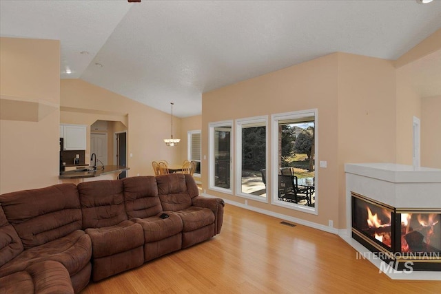 living room with light wood finished floors, visible vents, vaulted ceiling, and a tiled fireplace