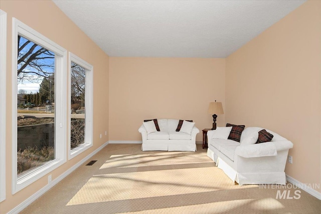 living area with a textured ceiling, carpet flooring, visible vents, and baseboards