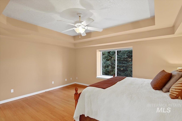 bedroom featuring a raised ceiling, baseboards, a textured ceiling, and light wood finished floors