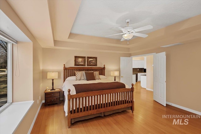 bedroom with a tray ceiling, visible vents, light wood-style flooring, a textured ceiling, and baseboards