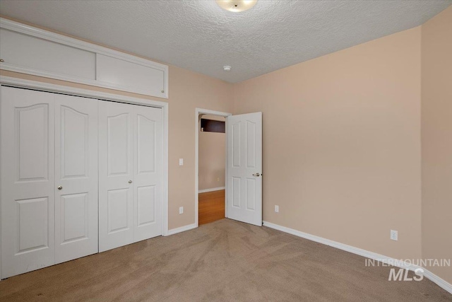 unfurnished bedroom featuring light carpet, a closet, a textured ceiling, and baseboards