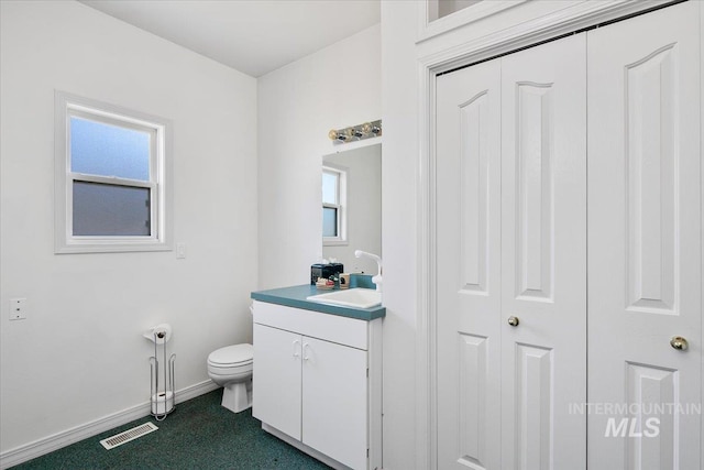 half bathroom with toilet, a healthy amount of sunlight, baseboards, and vanity