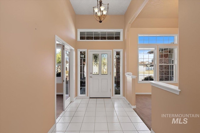 foyer entrance with light tile patterned flooring, plenty of natural light, a towering ceiling, and baseboards