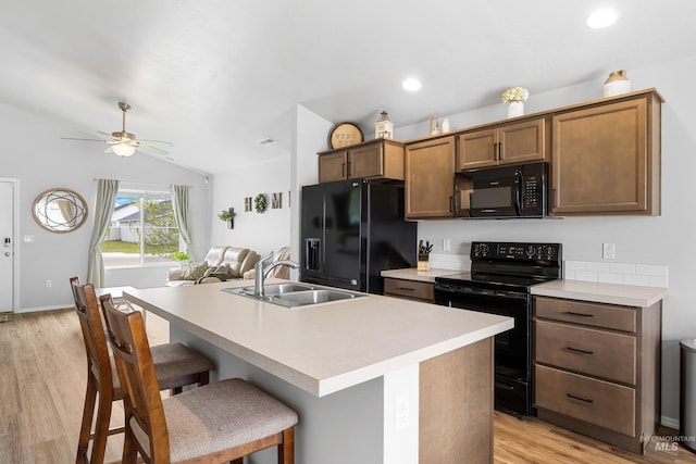 kitchen featuring a breakfast bar, a sink, light wood-style floors, light countertops, and black appliances