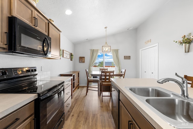 kitchen featuring a sink, light wood-style floors, decorative light fixtures, vaulted ceiling, and black appliances